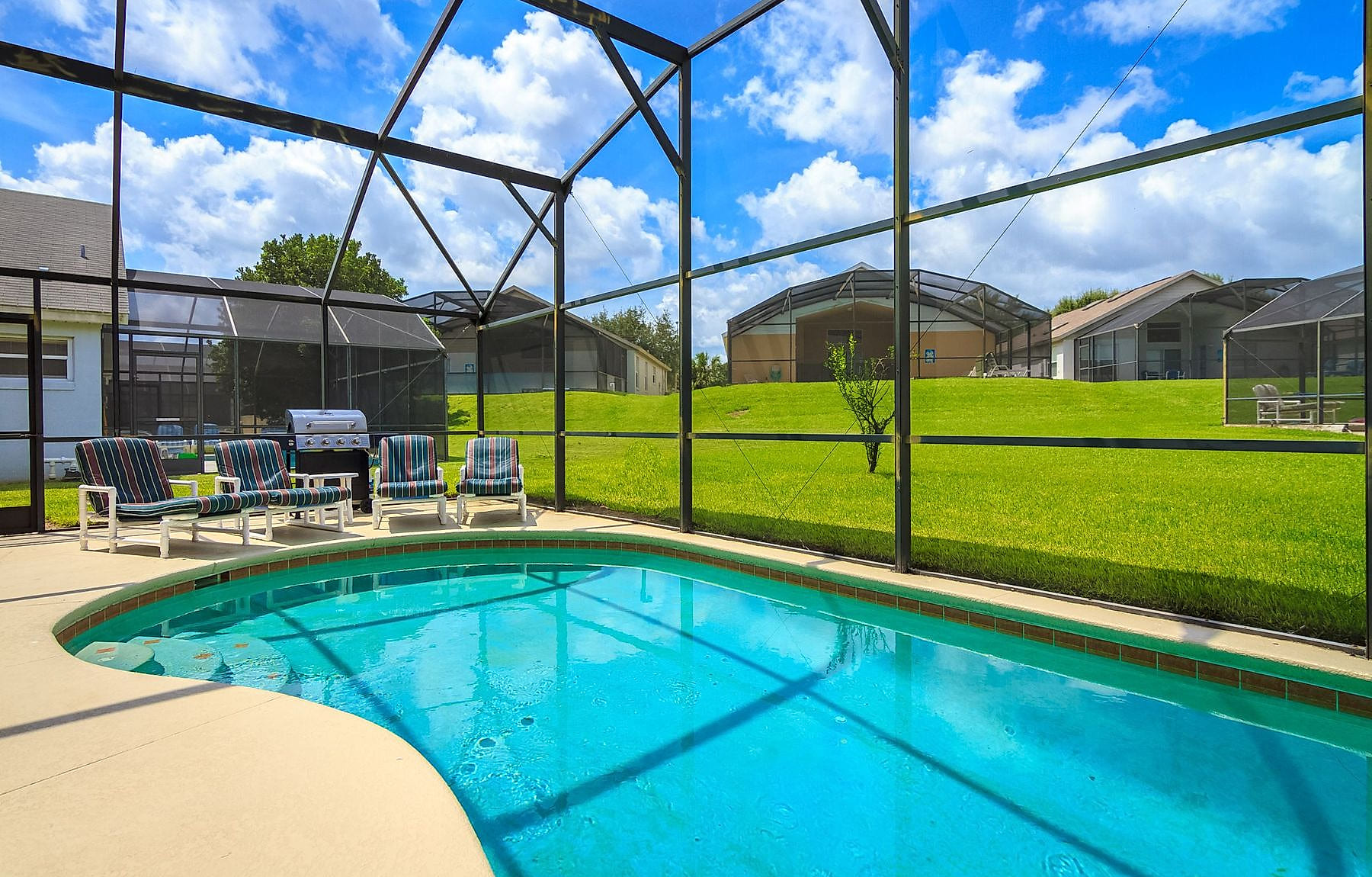 A screened pool cage over a blue swimming pool in Southwest Florida, lawn and neighbouring homes beyond